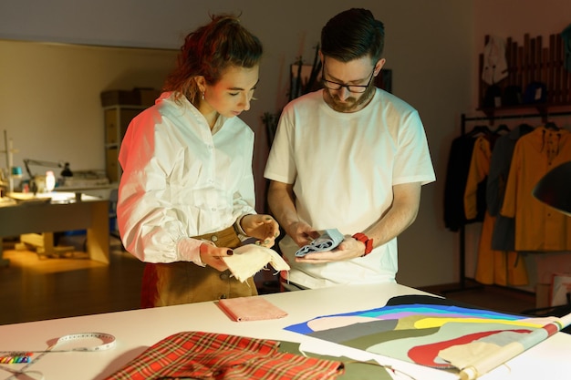Dressmakers choosing cloth fabric for clothes collection seamstress female talking to designer man